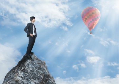 man standing on mountain looking at hot air balloon